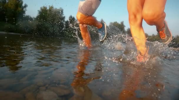 SUPER SLOW MOTION: Athletic couple running in shallow river water on sunny day. — ストック動画