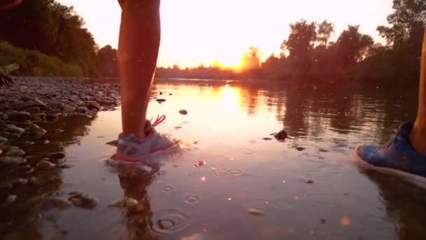MOCIÓN LENTA: Gotas de agua cristalinas vuelan como jogs de pareja atlética en un río poco profundo . — Vídeos de Stock