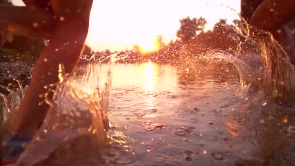 CHIUDI Donna e uomo irriconoscibili che corrono verso il tramonto e spruzzano acqua — Video Stock