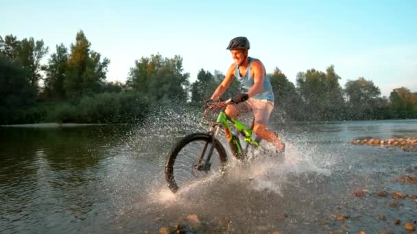 Pomalý pohyb: Veselý horský cyklista na koni v potoce a stříkající vody. — Stock video