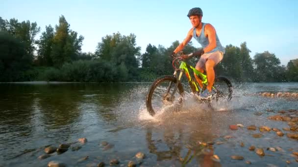 Time Warp: Šťastný horský cyklista na koni v mělké řece za slunečného večera. — Stock video