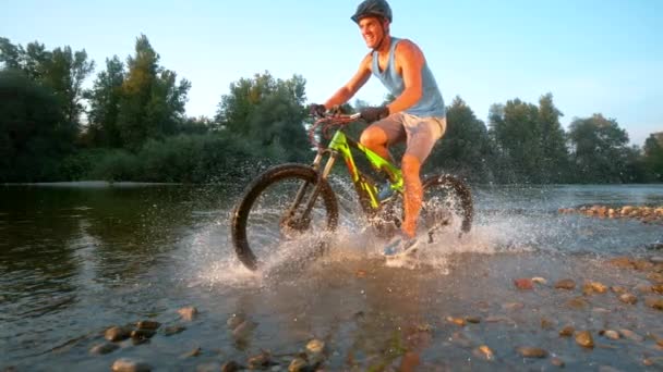 SUPER SLOW MOTION: Athletic cross country biker riding along a shallow stream.