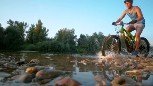 LOW ANGLE: Aktiv man rider sin mountainbike och stänk uppfriskande vatten. — Stockvideo