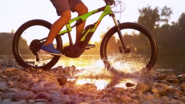 SUN FLARE: Unrecognizable sportsman riding a mountain bike in a shallow stream.