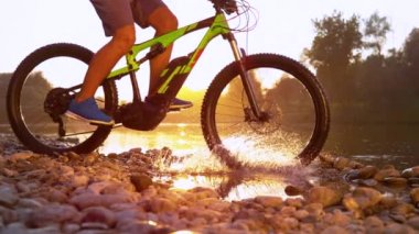 SLOW MOTION CLOSEUP Unrecognizable man MTB biking in shallow river at sunset