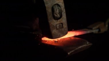 SLOW MOTION, MACRO, DOF: Bright orange steel blade getting forged by unrecognizable craftsman. Tiny particles flying away from glowing hot blade after getting struck by a heavy blacksmith's hammer