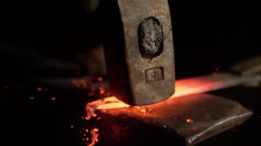 SLOW MOTION, MACRO, DOF: Bright orange steel blade getting forged by unrecognizable craftsman. Tiny particles flying away from glowing hot blade after getting struck by a heavy blacksmith's hammer