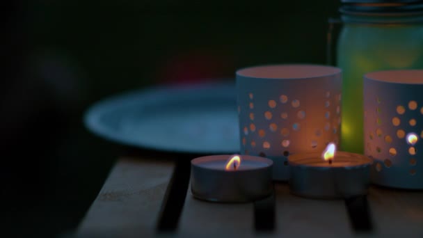 MACRO: Velas pequeñas parpadean en la mesa de jardín de madera en una noche de verano . — Vídeo de stock