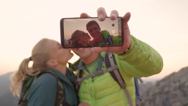 CLOSE UP: Ung kvinna i kärlek kysser sin lyckliga pojkvän medan du tar en selfie. — Stockvideo