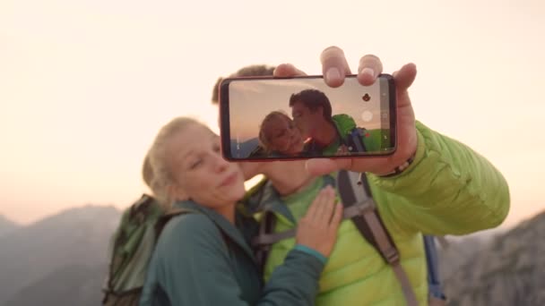 Movimiento lento: El hombre se toma una selfie de él besando a su novia en la mejilla al atardecer . — Vídeos de Stock