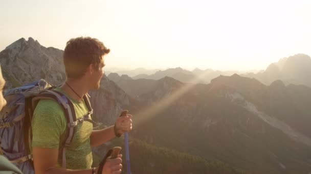 Lassú mozgás: fiatal pár áll a hegytetőn, és nézi a naplementét. — Stock videók