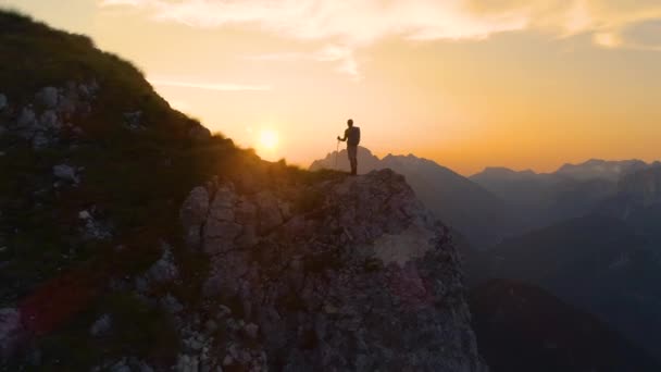 LENS FLARE: lenyűgöző naplemente megvilágítja az Alpok és túrázó álló egy sziklán. — Stock videók