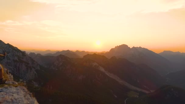 Antenn: Spännande vandrare sträcker ut armarna när han tittar på solnedgången från en klippa. — Stockvideo
