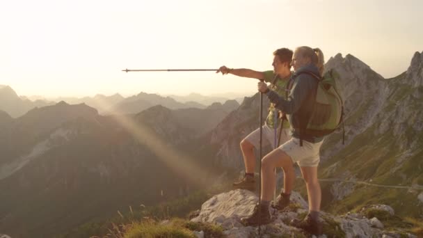 MOVIMIENTO Lento: Pareja activa observa la puesta de sol desde un pico de montaña en los Alpes . — Vídeo de stock