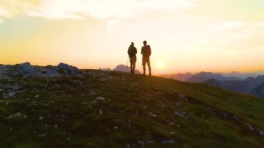 DRONE: Stunning golden sunrise shines on the mountains and excited man and woman