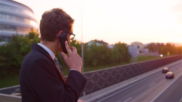 Nahaufnahme: Yuppie telefoniert mit seinem Chef beim Blick auf die Autobahn — Stockvideo