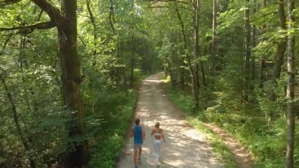 AERIAL: Lecąc za nierozpoznawalną dopasowaną parą biegającą ścieżką leśną. — Wideo stockowe