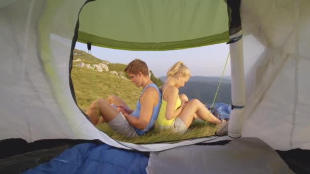 CLOSE UP: Mann und Frau lehnen sich gegenseitig auf den Rücken und verschwenden Zeit mit Telefonen — Stockvideo