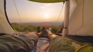Genç çift çadırdan gün batımını izlerken ayaklarını hareket ettiriyor.