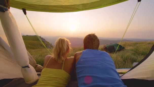 Mladý pár turistů ležící ve stanu a pozorující západ slunce. — Stock video