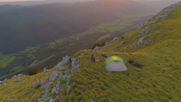 DRONE: Toeristisch koppel zit en knuffelt bij de tent op een zonnige zomeravond — Stockvideo