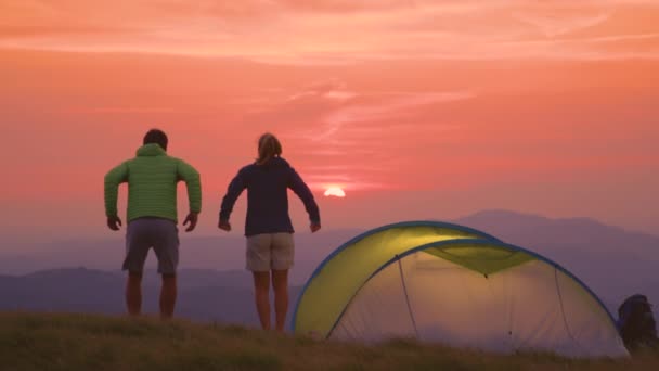 慢动作：在阿尔卑斯山的一个阳光灿烂的夜晚，露营者跳跃着，伸展着双臂. — 图库视频影像