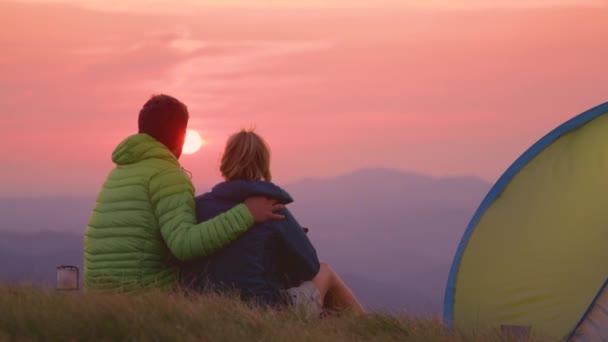 FECHAR UP: Casal abraçando nas montanhas com seu filhote de cachorro e assistindo o pôr do sol — Vídeo de Stock