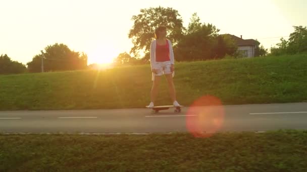 LENS FLARE: Fröhliche Frau fährt an einem sonnigen Tag mit dem Skateboard durch den Park. — Stockvideo