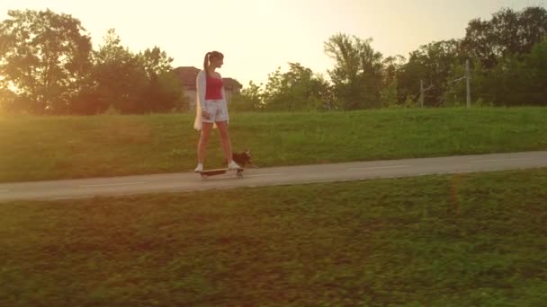 Movimiento lento: Pinscher en miniatura corre a lo largo de la mujer feliz montando su longboard . — Vídeo de stock