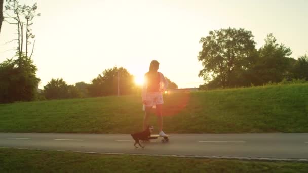 SLOW MOTION: Fata lipsită de griji luând câinele ei pentru o plimbare în timp ce ea merge pe o placă lungă — Videoclip de stoc