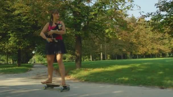 Movimiento lento: Mujer feliz sosteniendo a su perro senior mientras monta su e-skateboard . — Vídeos de Stock