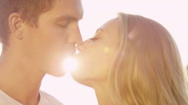 Yavaş çekim altın güneş ışığı, sevgilisini burnundan öperken erkeğin üzerinde parlıyor.