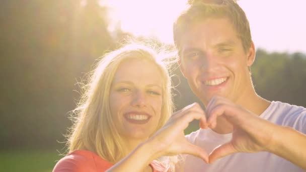 느린 동작: 행복 한 부부가 심장의 상징을 만드는 동안 카메라를 들여다보고 있다. — 비디오