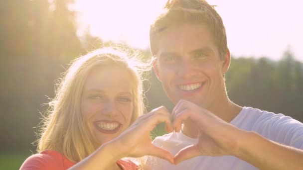 ПОРТРАЙТ: Серьёзная пара, создающая форму сердца с пальцами, улыбающимися в камеру . — стоковое видео