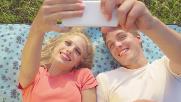 CLOSE UP Cheerful young couple lying on a blanket and taking selfies during date — Stock Video