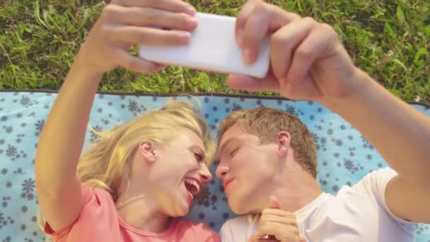 CLOSE UP: Adorable newlyweds kiss as they lie on the blanket and take selfies. — Stock Video