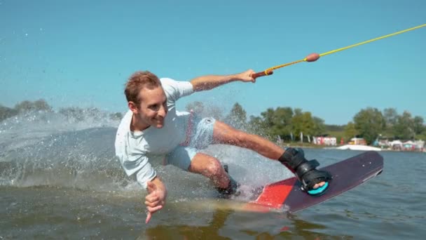 FECHAR UP: Sorrindo wakeboarder cara dá o sinal de shaka como ele surfa câmera passada. — Vídeo de Stock