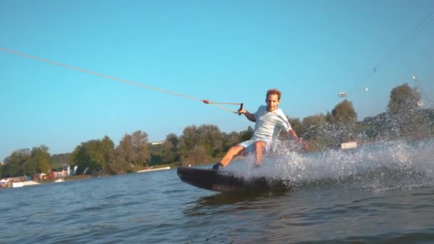 スローモーション:穏やかな湖の男のウェイクスーフとしてカメラで飛ぶ水のガラス滴. — ストック動画