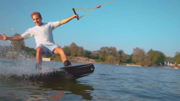 SLOW MOTION, CLOSE UP: Fit young man smiles as he wakesurfs past the camera. — Stock Video