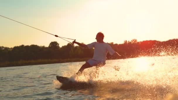 FLARE DE LA LENTE: Hombre feliz divirtiéndose wakeboarding en el parque de cable fresco al amanecer . — Vídeo de stock