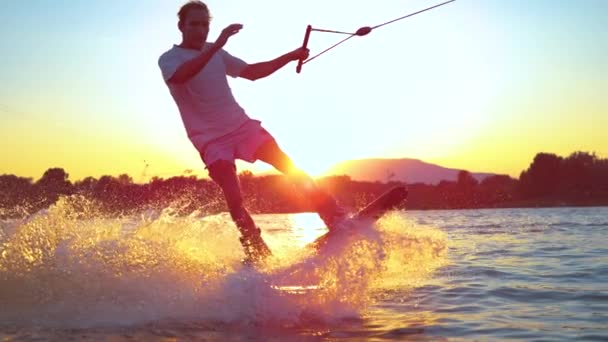 SLOW MOTION FLOSE UP: Surfista jovem wakeboarding e salto 180 ollie ao pôr do sol — Vídeo de Stock