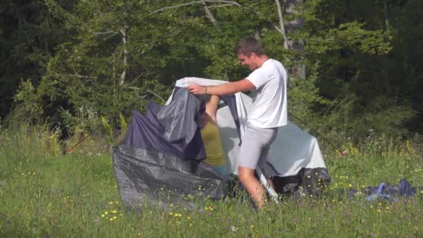 Playful tourist couple having problems setting up their tent by the calm forest. — Stock Video