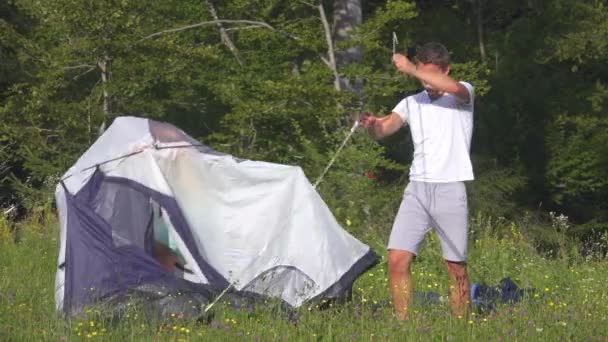 Młody człowiek denerwuje się, gdy para turystów ma problemy z rozłożeniem namiotu. — Wideo stockowe