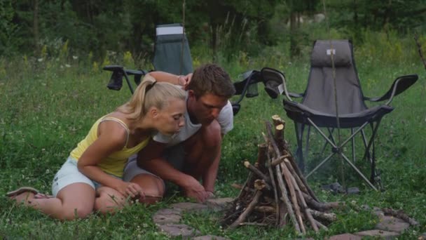 CLOSE UP: Happy couple blowing at the burning tinder to light up a campfire. — Stock Video