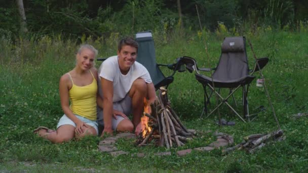 PORTRAIT: Šťastný cestovatel pár sedí u táboráku v letním večeru. — Stock video