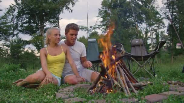 CLOSE UP: Blondes Mädchen schaut ihren Freund an, wie er mit einem Stock das Feuer ansticht — Stockvideo