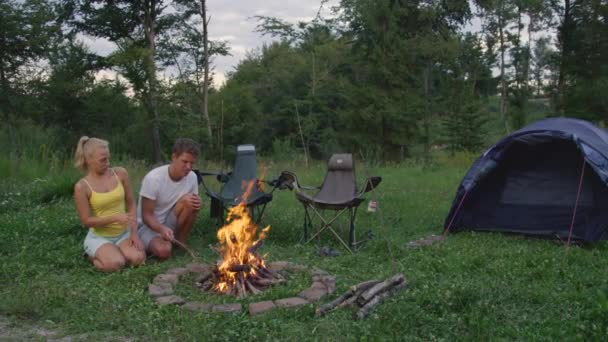 Młody mężczyzna i kobieta siedzący przy ognisku irytują się brzydkimi robalami. — Wideo stockowe