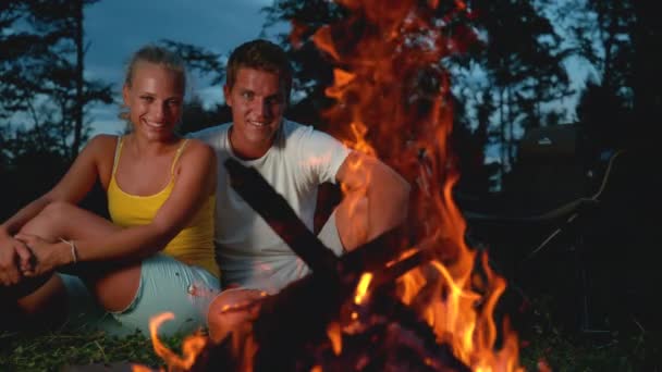 Zeitlupe: Lächelnde Frau und Mann sitzen am Lagerfeuer und verlieren sich in Gedanken. — Stockvideo