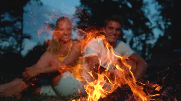 CLOSE UP: Sparks come flying out of a campfire as tourist couple sits nearby. — Stock Video