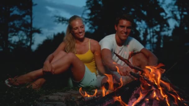 Zeitlupe: Fröhlicher Mann sticht beim Zelten mit Freundin mit Stock in Feuer. — Stockvideo